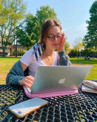 Senior Isa Sanchez is sitting at a picnic table in the Campus Green. She's working on her laptop. 